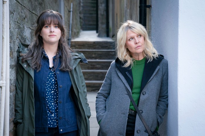 Alison O'Donnell as Tosh and Ashley Jensen as Ruth in Shetland, standing next to one another in the town in front of some steps